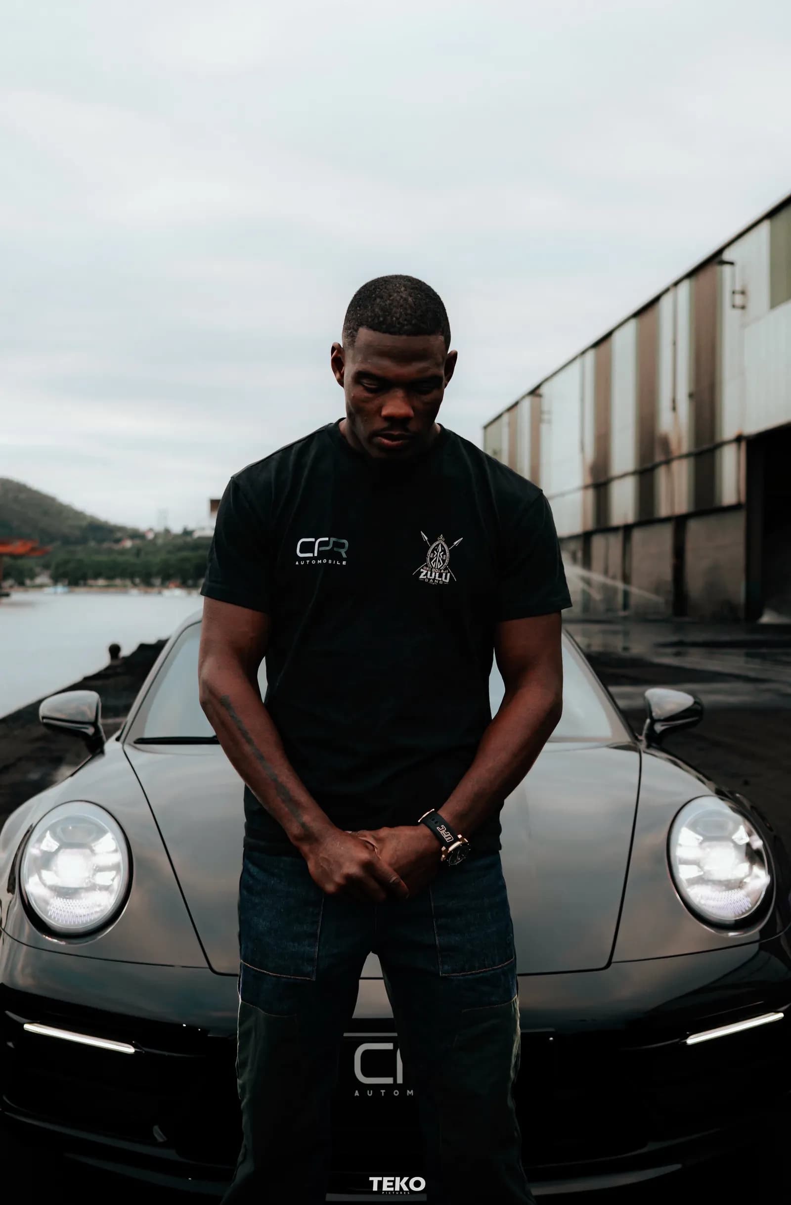 Oki Bolaji en tee Zulu Gang, devant une Porsche
